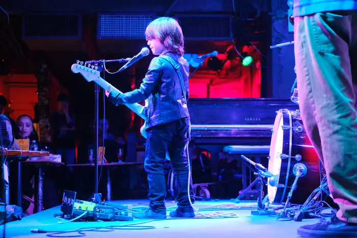 A small boy playing electric guitar onstage